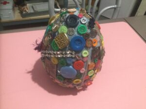 large ceramic egg with buttons and jewelry glued all over it